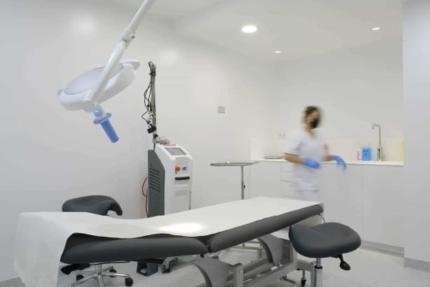 sala de atención dermatológica con una camilla negra y una dermatóloga en movimiento