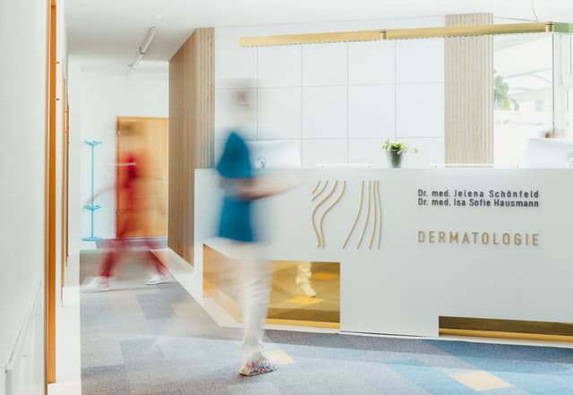 Hautarztpraxis Schönfeld & Hausmann. Eine Schwester läuft am Tresen vorbei 