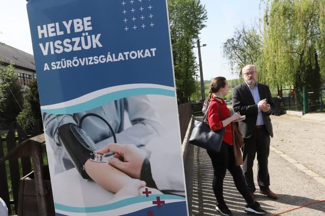 Helyszíni egyeztetés: Dr. Laczkó Tamás a "Helybe visszük a szűrővizsgálatokat" feliratú kék tábla mellett beszélget.