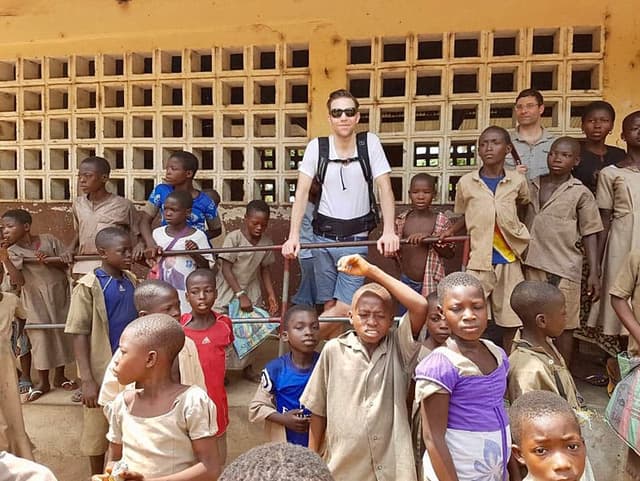 Eine Gruppe von Kindern in Schuluniformen steht vor einem Gebäude mit zwei Erwachsenen.