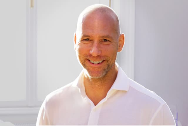 Dr. Oliver Kandel lächelt und trägt ein weißes Hemd.