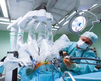 Ein Chirurg bedient ein robotergestütztes Operationssystem in einem Operationssaal, während er ein chirurgisches Instrument hält. Der Chirurg trägt eine Maske und sterile Kleidung, um eine sichere Umgebung zu gewährleisten.