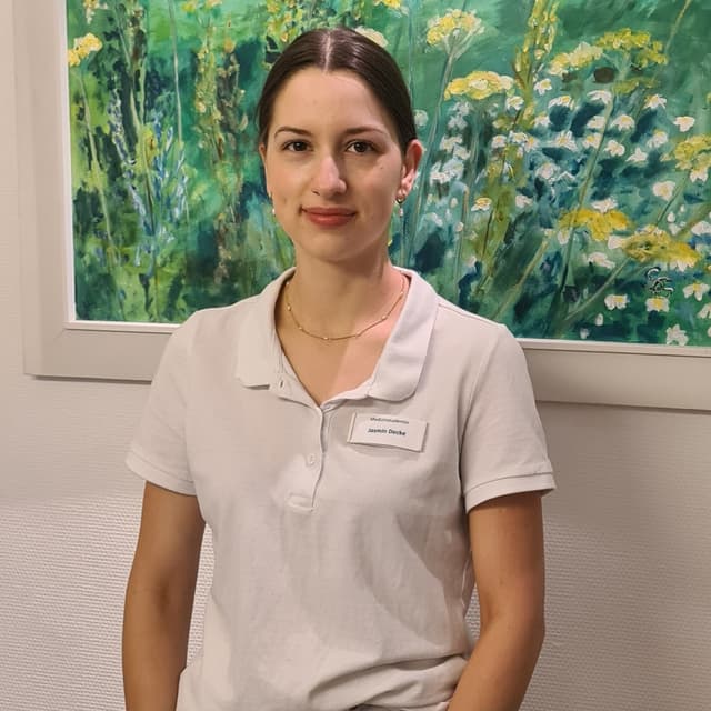 Jasmin in weißem Polohemd vor einem Gemälde mit Blumenmotiv