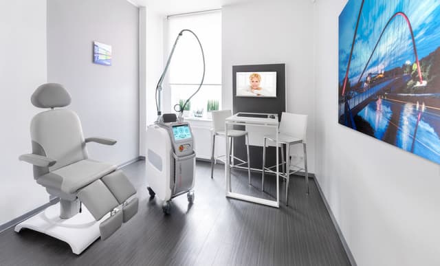 Behandlungsraum mit Stuhl, Lasergerät, Monitor, und Kunstwerk an der Wand.